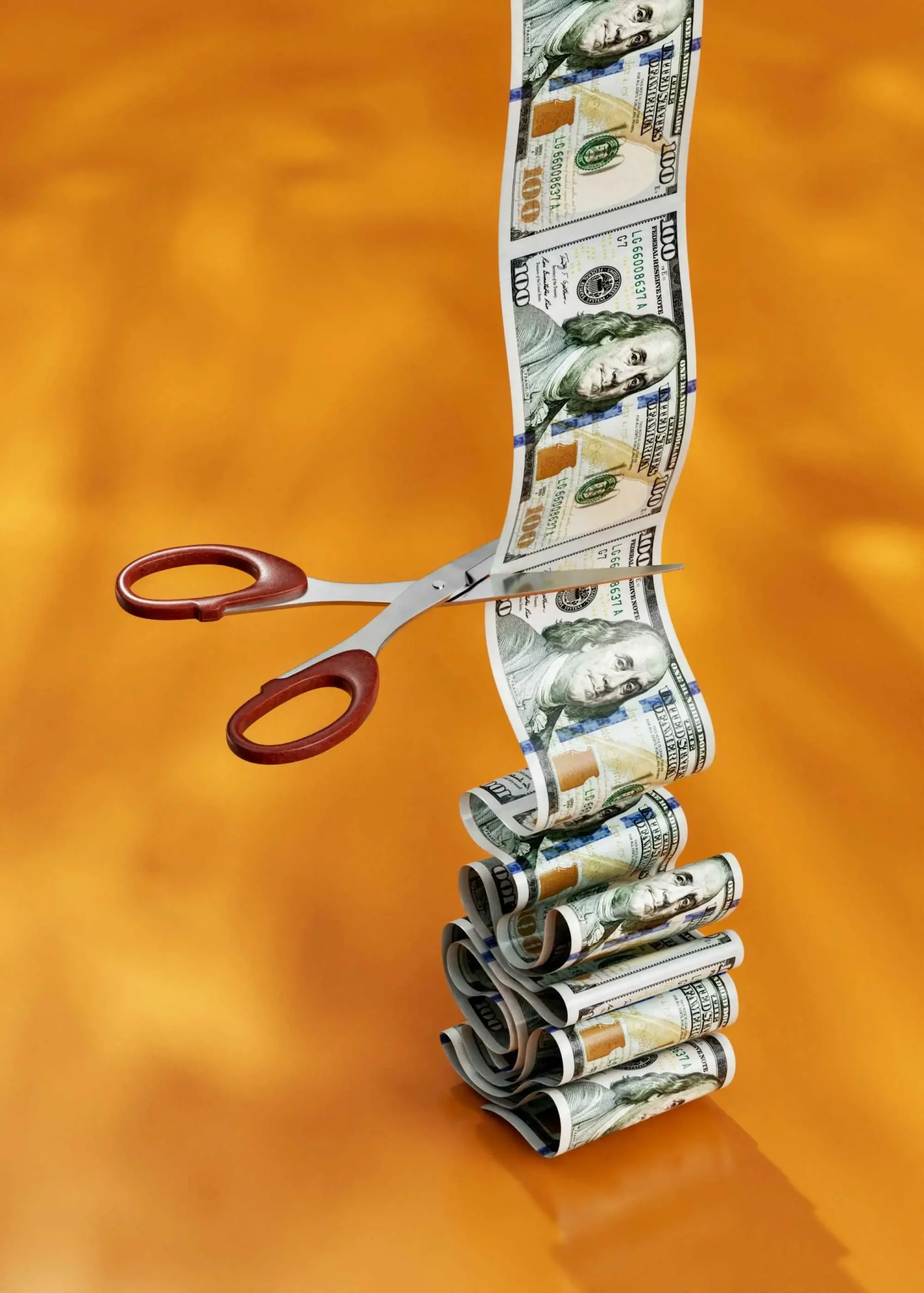 Scissors cutting stack of hundred-dollar bills.