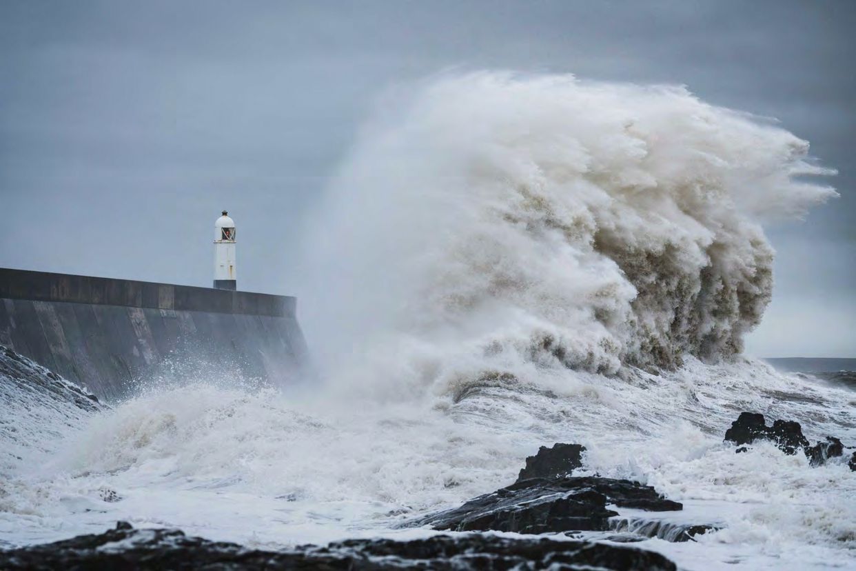 Huge wave crashing against lighthouse and seawall